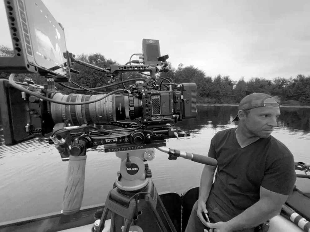 Stefan Szary on a camera boat beside a cinema camera on a tripod